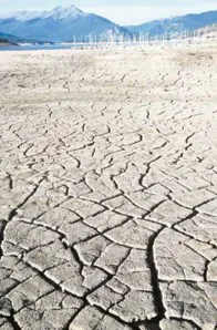 The image shows a dry, cracked landscape, suggesting drought conditions, with mountains and wind turbines in the background.
