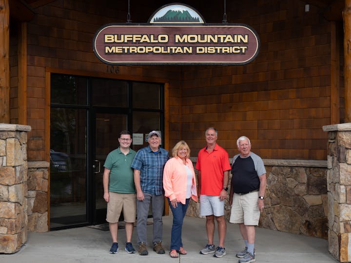 Five people standing in front of the "Buffalo Mountain Metropolitan District" sign outside a building.