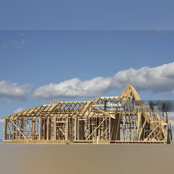 A wooden structure in the frame of a house under construction, set against a blue sky with clouds.