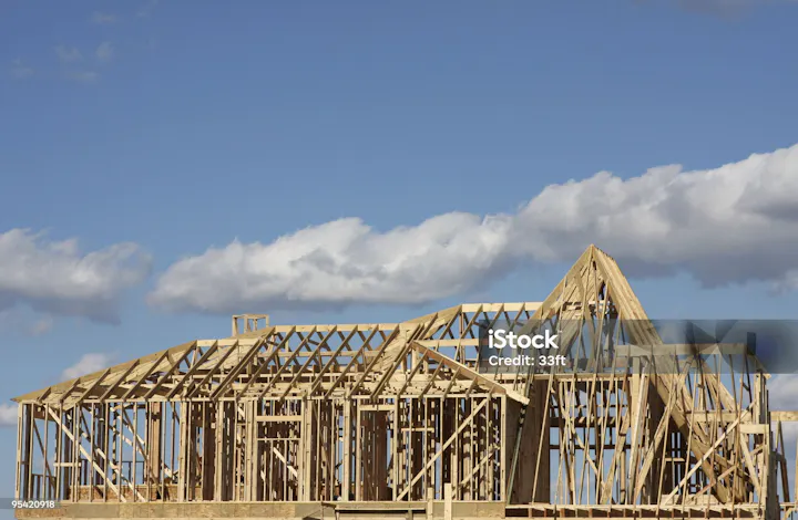 A wooden structure in the frame of a house under construction, set against a blue sky with clouds.