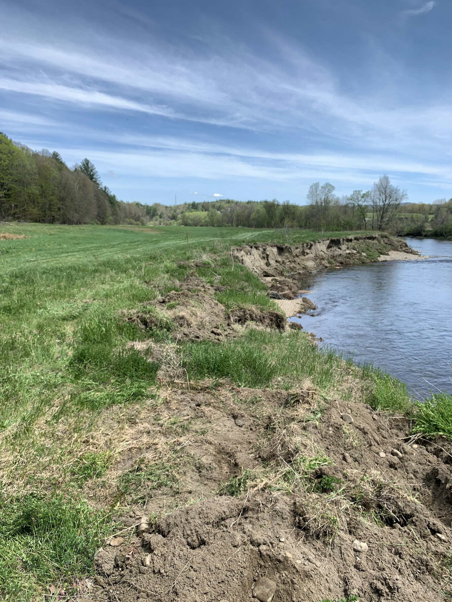 A river with grassy banks under a partly cloudy sky.