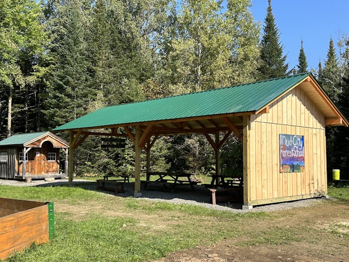 A covered outdoor area with picnic tables and a sign "MudCity ForestSchool," surrounded by trees.