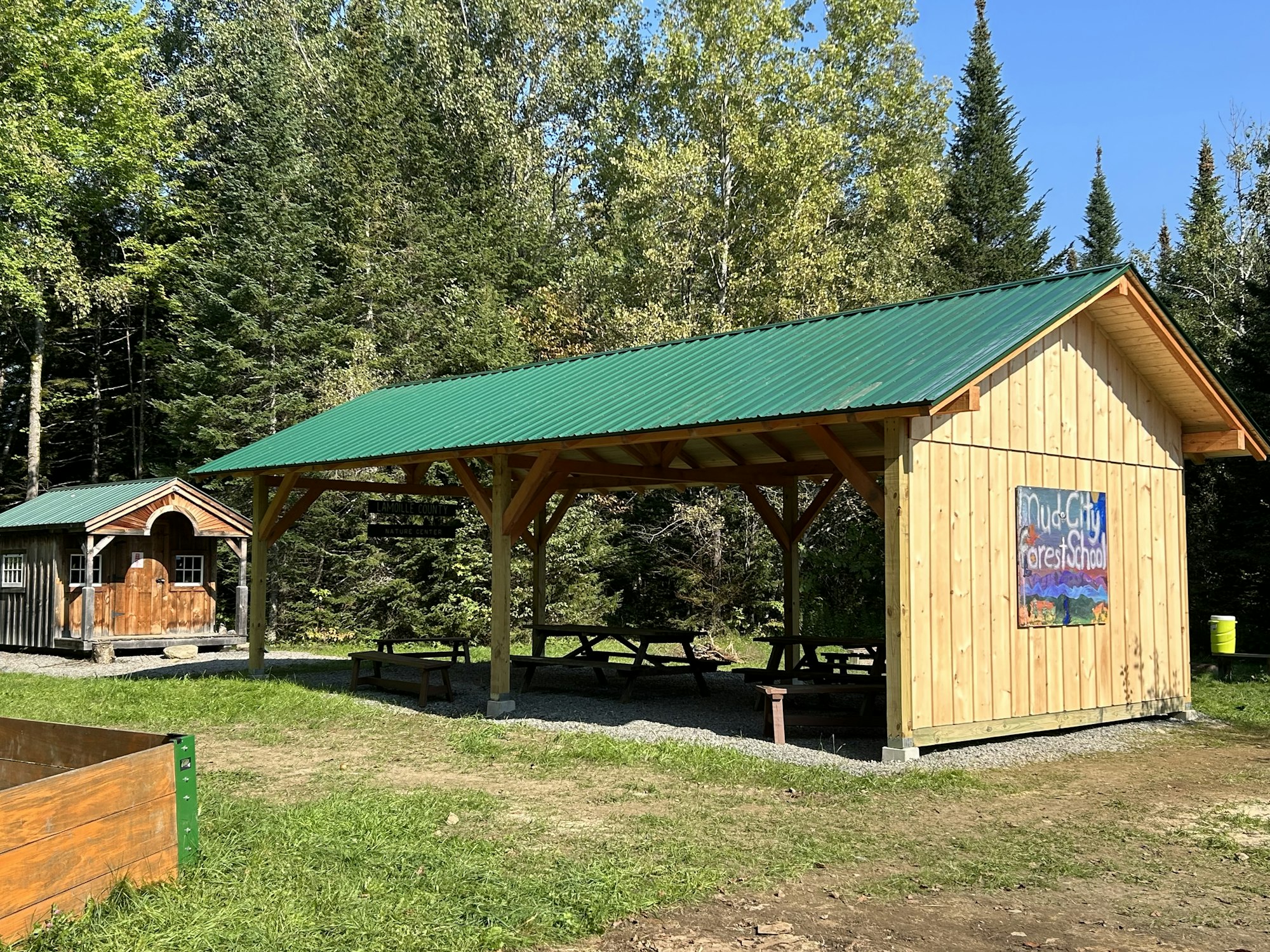 A covered outdoor area with picnic tables and a sign "MudCity ForestSchool," surrounded by trees.