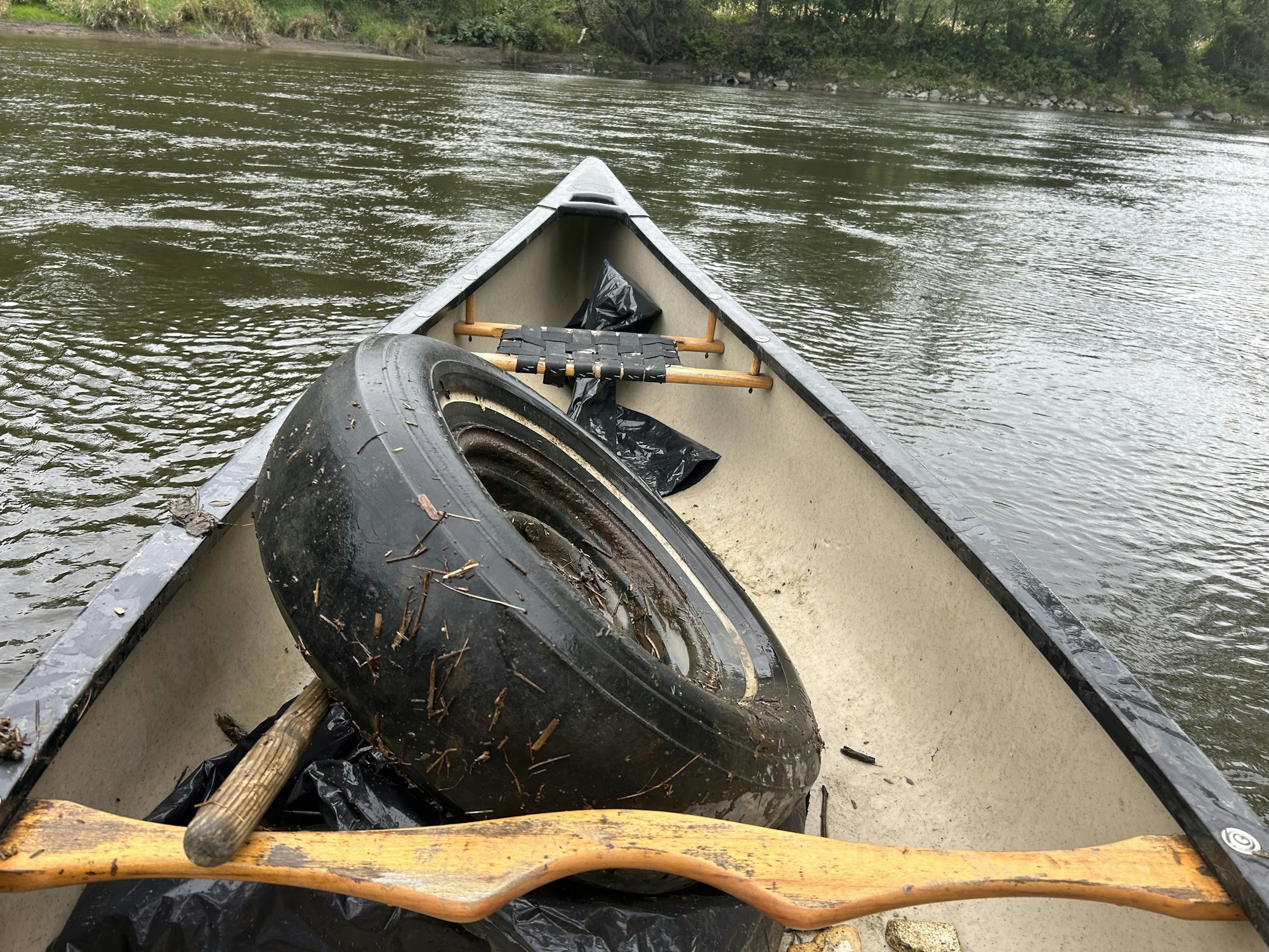 A canoe with a tire, oar, and debris on a river.