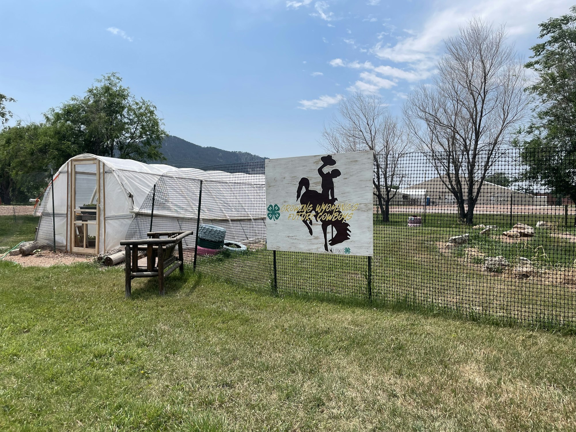A greenhouse, a sign with a cowboy silhouette, a fenced area, and a mountainous background.