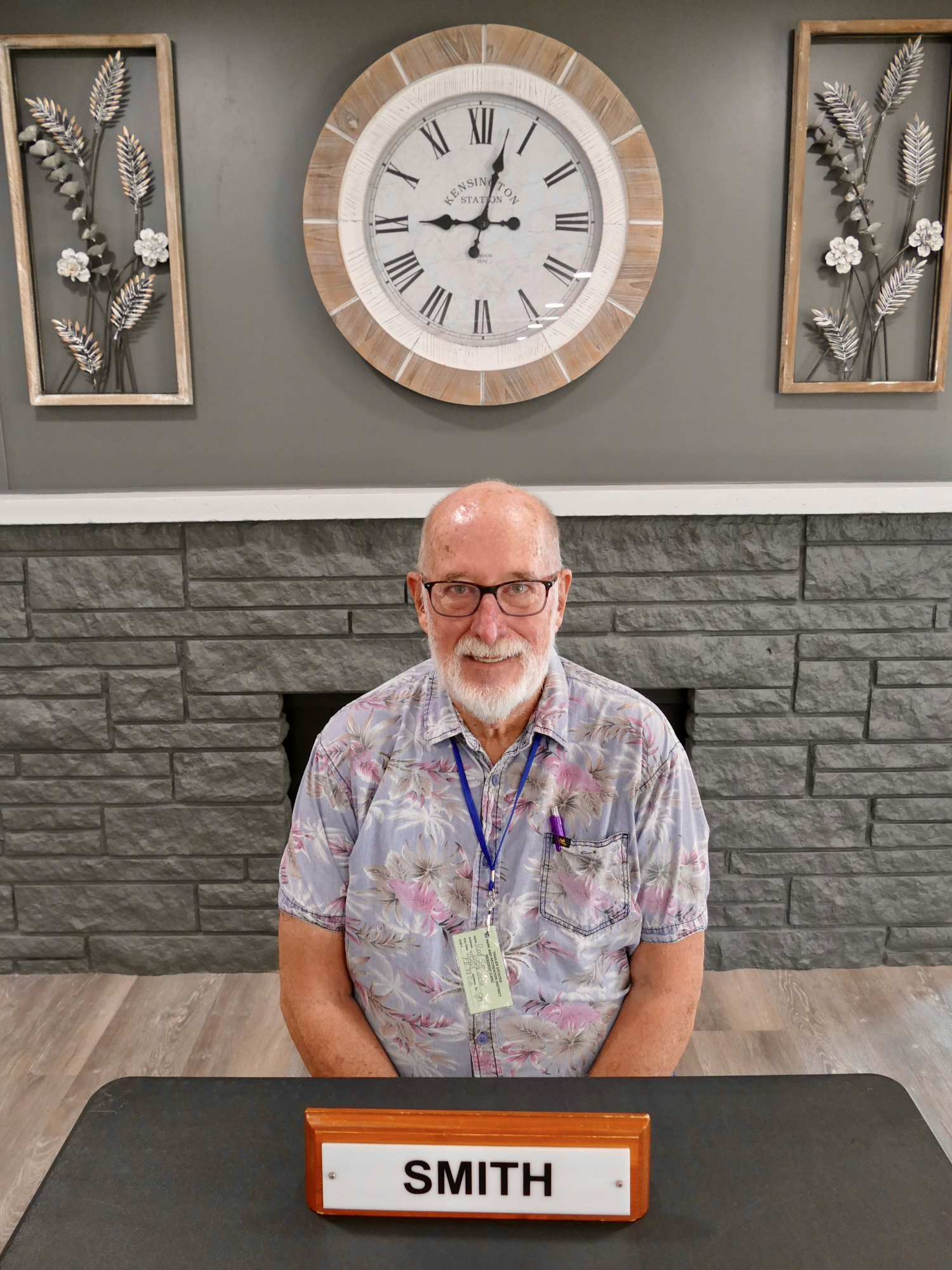 May contain: face, head, person, photography, portrait, adult, male, man, furniture, table, accessories, glasses, analog clock, and clock