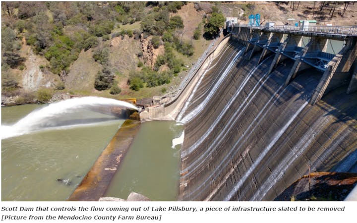 A dam releasing water, surrounded by natural terrain.