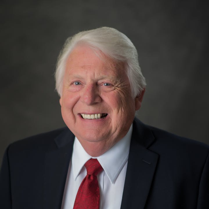 A smiling man in a suit and red tie poses for a portrait against a dark background.