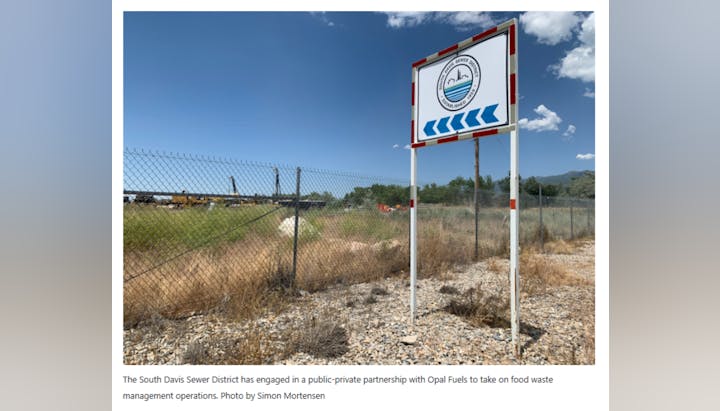 A sign for South Davis Sewer District near a fenced area under a clear sky by Simon Mortensen..
