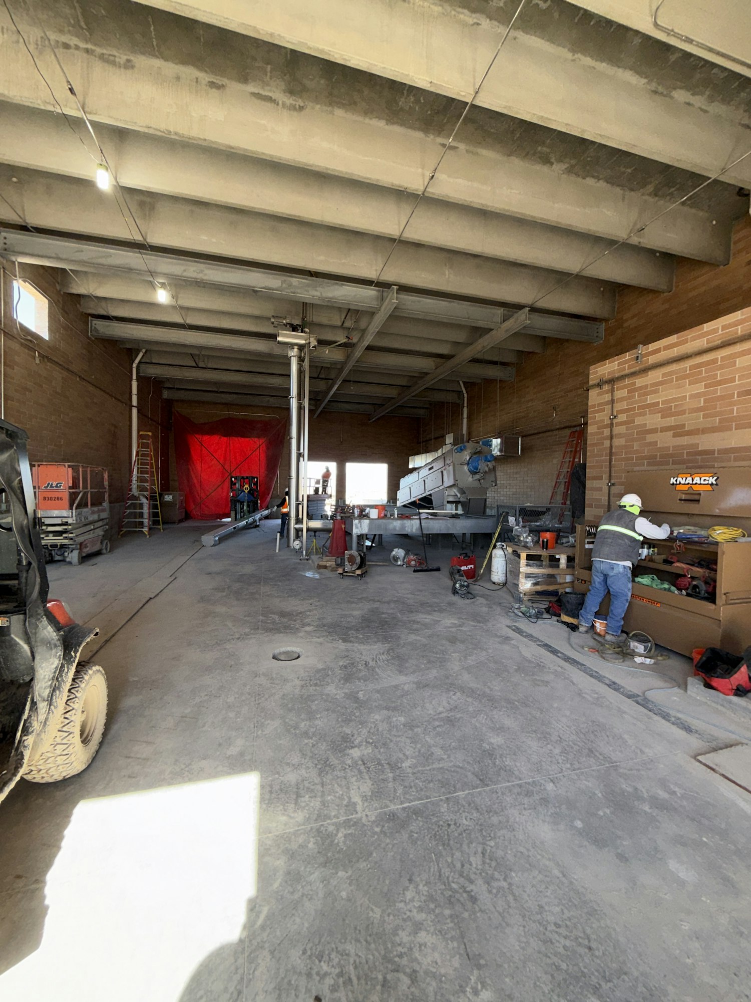 The image shows a construction or workshop area with equipment, tools, and a worker in a partially finished interior space.