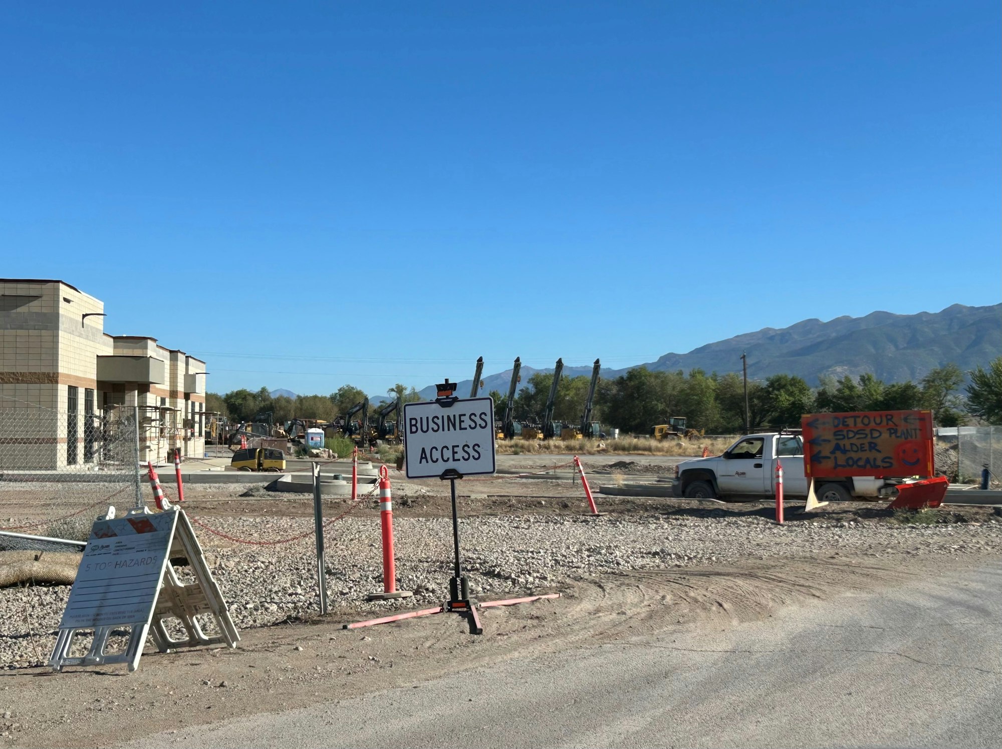 Construction site with signs for business access and a detour. Mountains in the background.