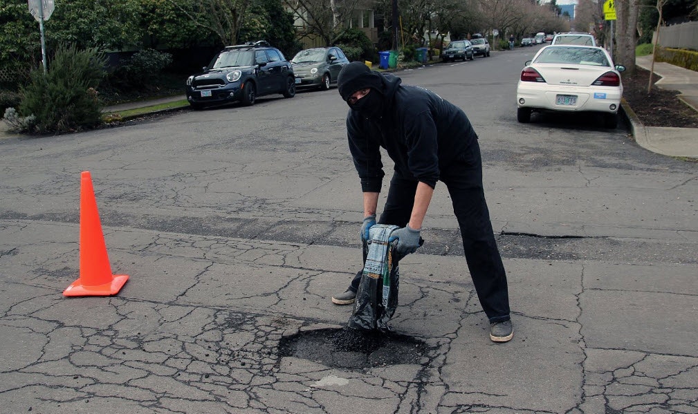 Worker patching road damage on a car lined street