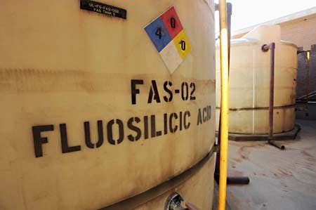 A large tank labeled "Fluosilicic Acid" with hazard symbols indicating safety information.