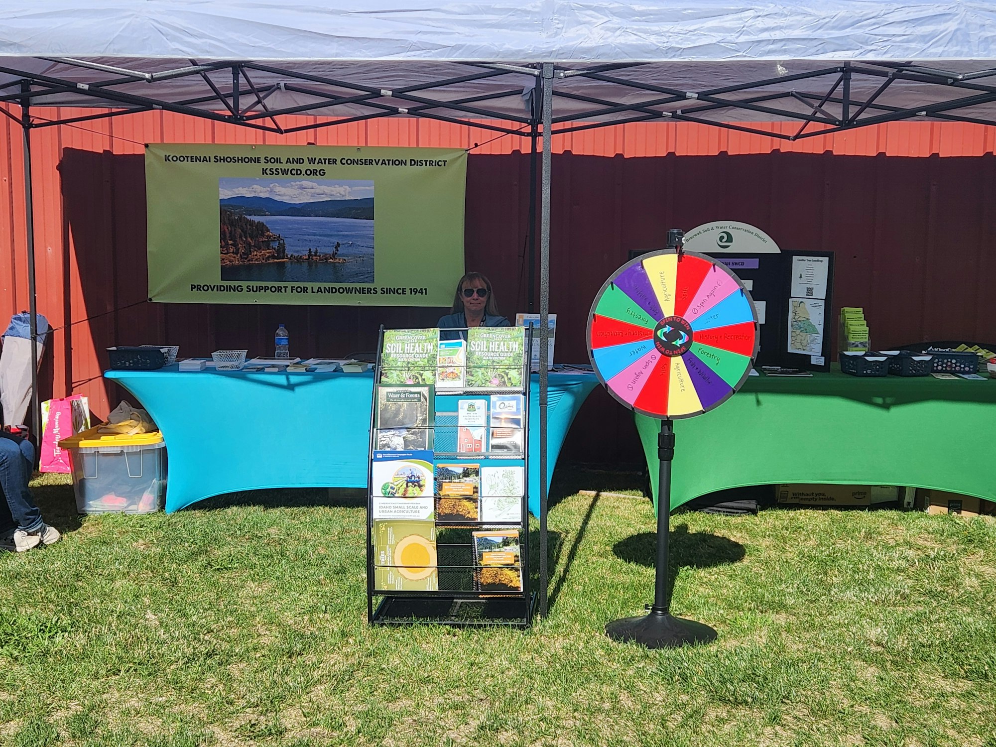 Outdoor booth with informative flyers, a spinning wheel, and a banner for Kootenai Shoshone Soil and Water Conservation District.