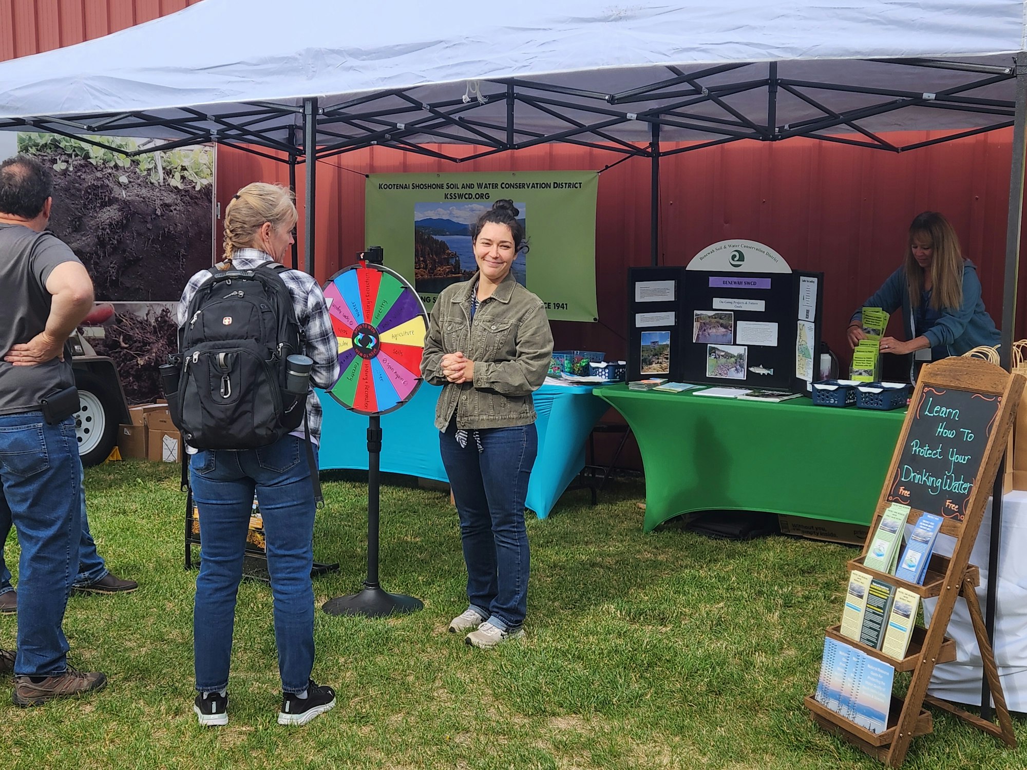 Outdoor booth with a spinning wheel game. People interacting, brochures available on drinking water protection.