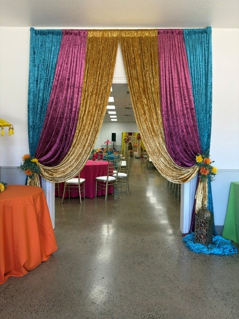A vibrant entrance draped with colorful fabric leads to a festive room with decorated tables and chairs.