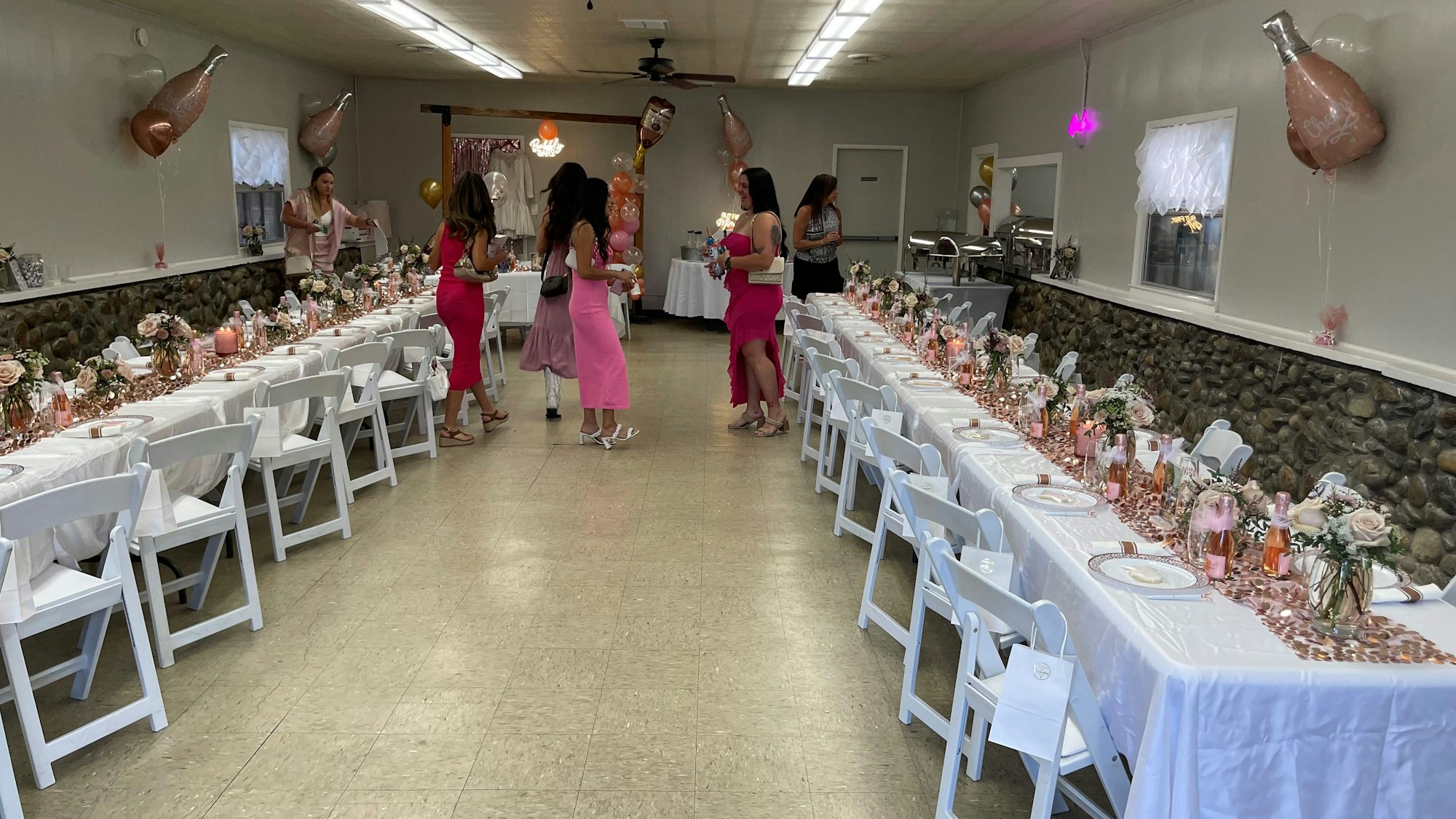 A decorated hall for an event with tables, chairs, balloons, and people gathered.