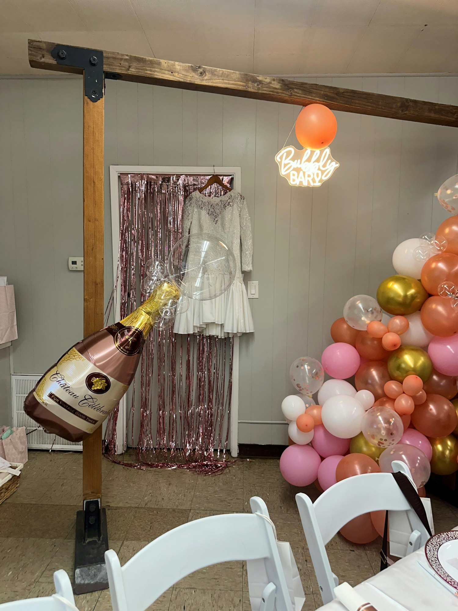 Party room with balloon decorations, a neon "Birthday" sign, and an oversized champagne bottle balloon.