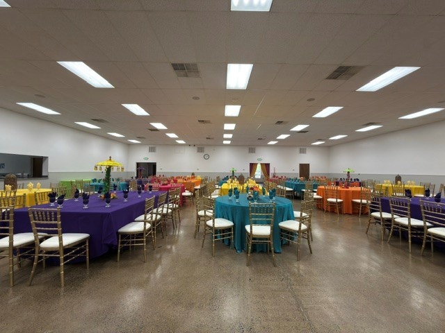 A spacious hall with brightly colored tables and chairs set up for an event, featuring gold accents and decorative centerpieces.