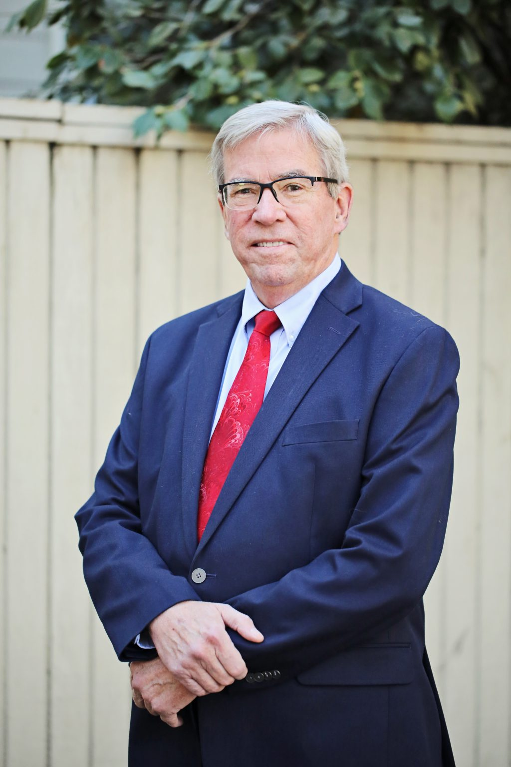 Man in suit with red tie standing by a fence; appears professional.