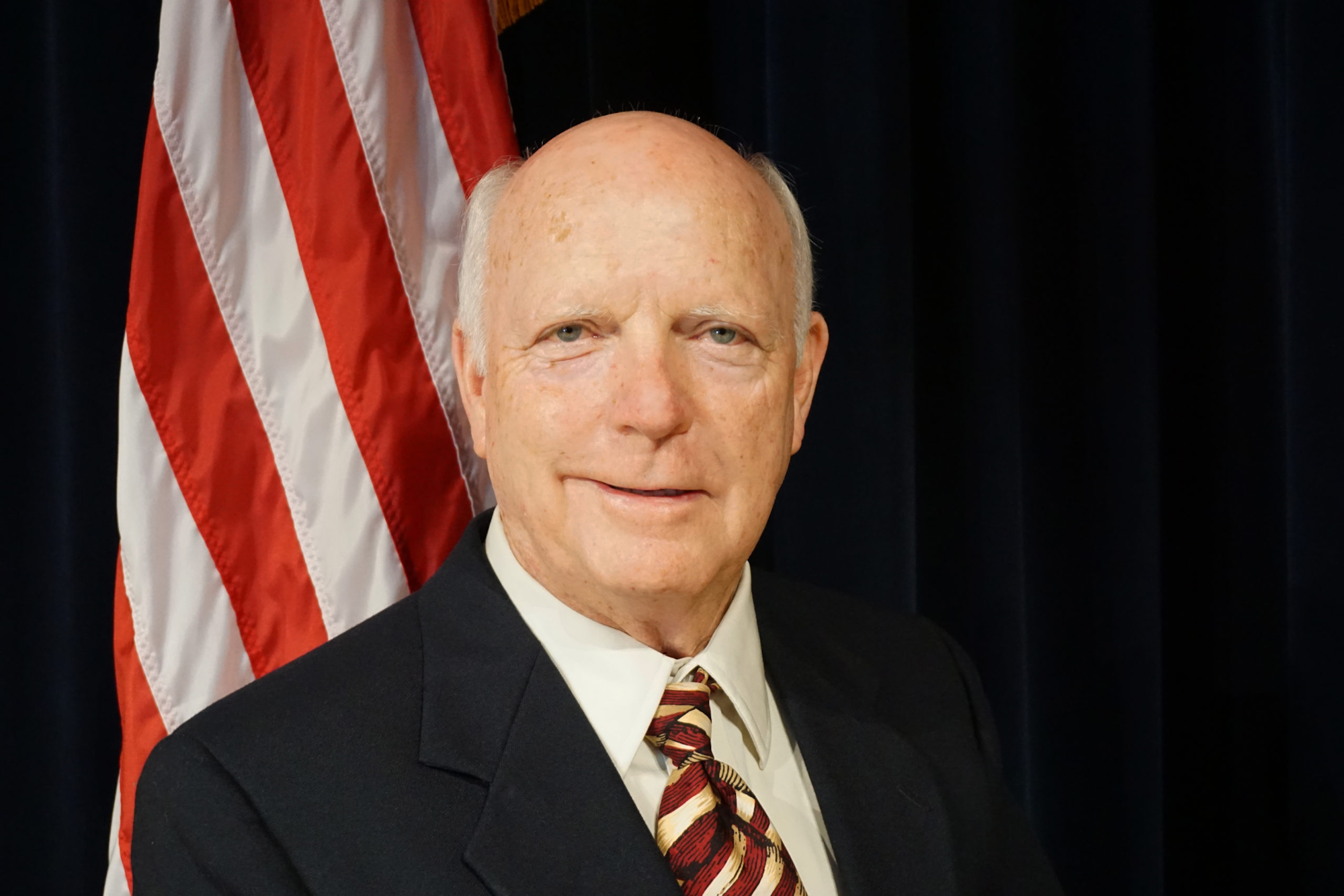 A man in a suit with an American flag in the background.