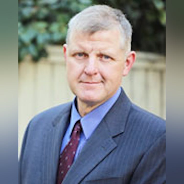 A man in a suit with a tie, having short grey hair, looking at the camera.