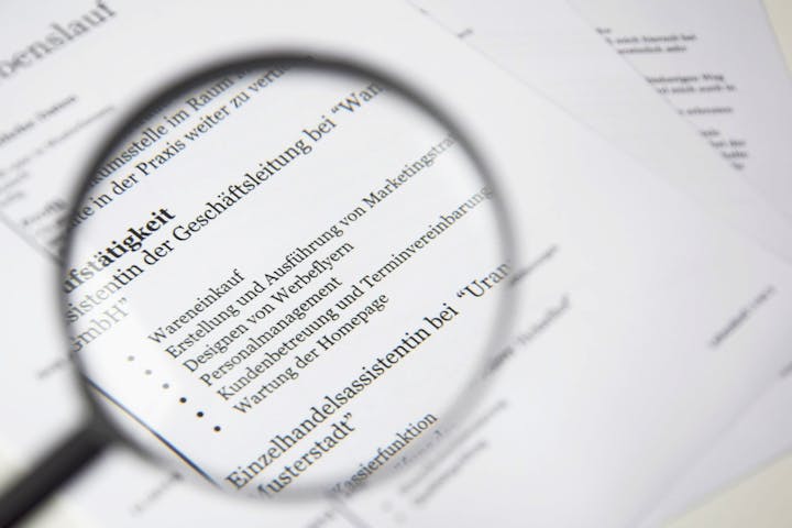 The image shows a magnifying glass over text from a document, likely a resume or job description in German.