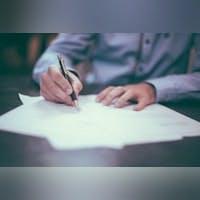 Person writing on paper, close-up on hands with pen, blurred background.