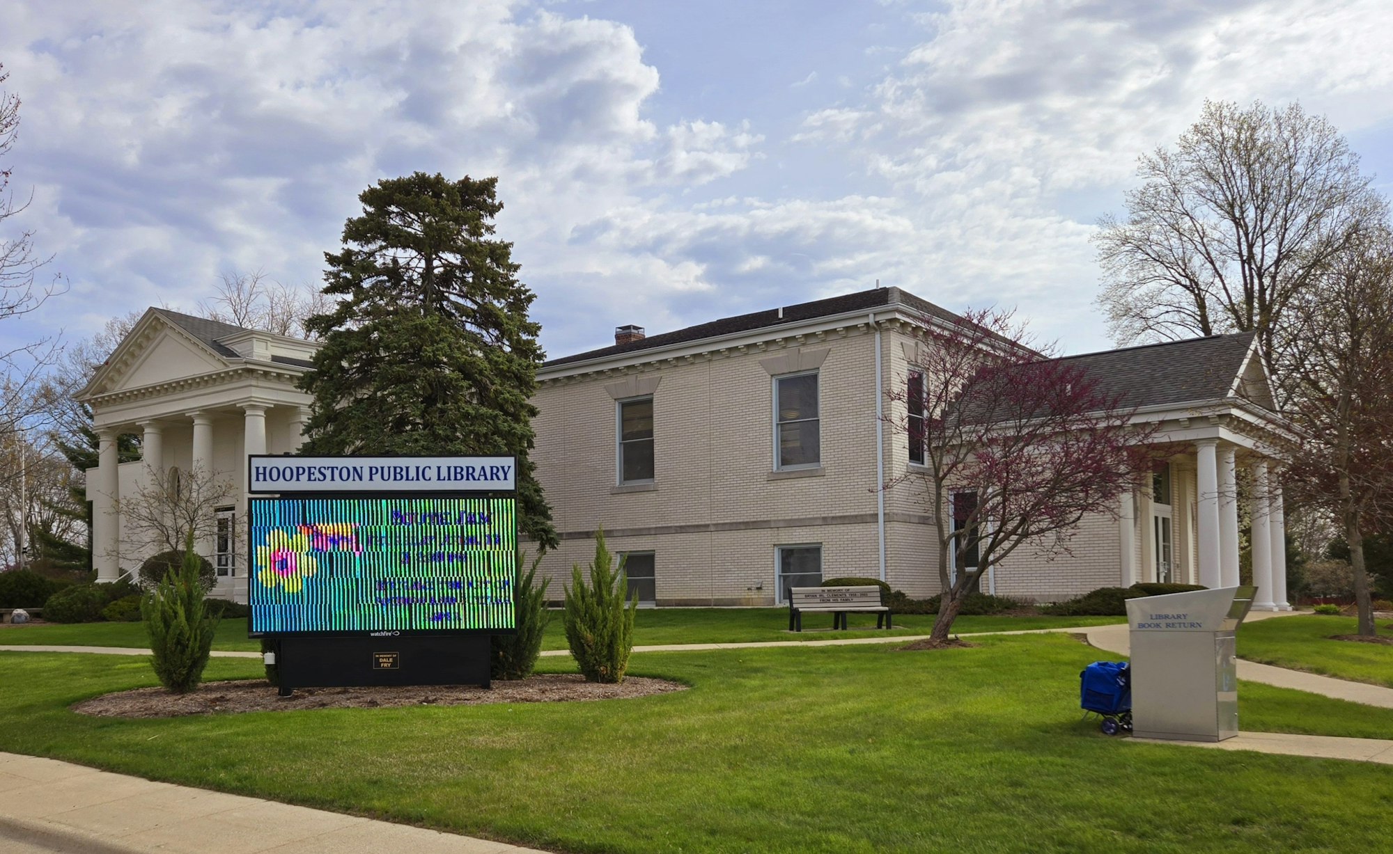 Hoopeston Public Library building with a digital sign, trees, and a book return station in the foreground.