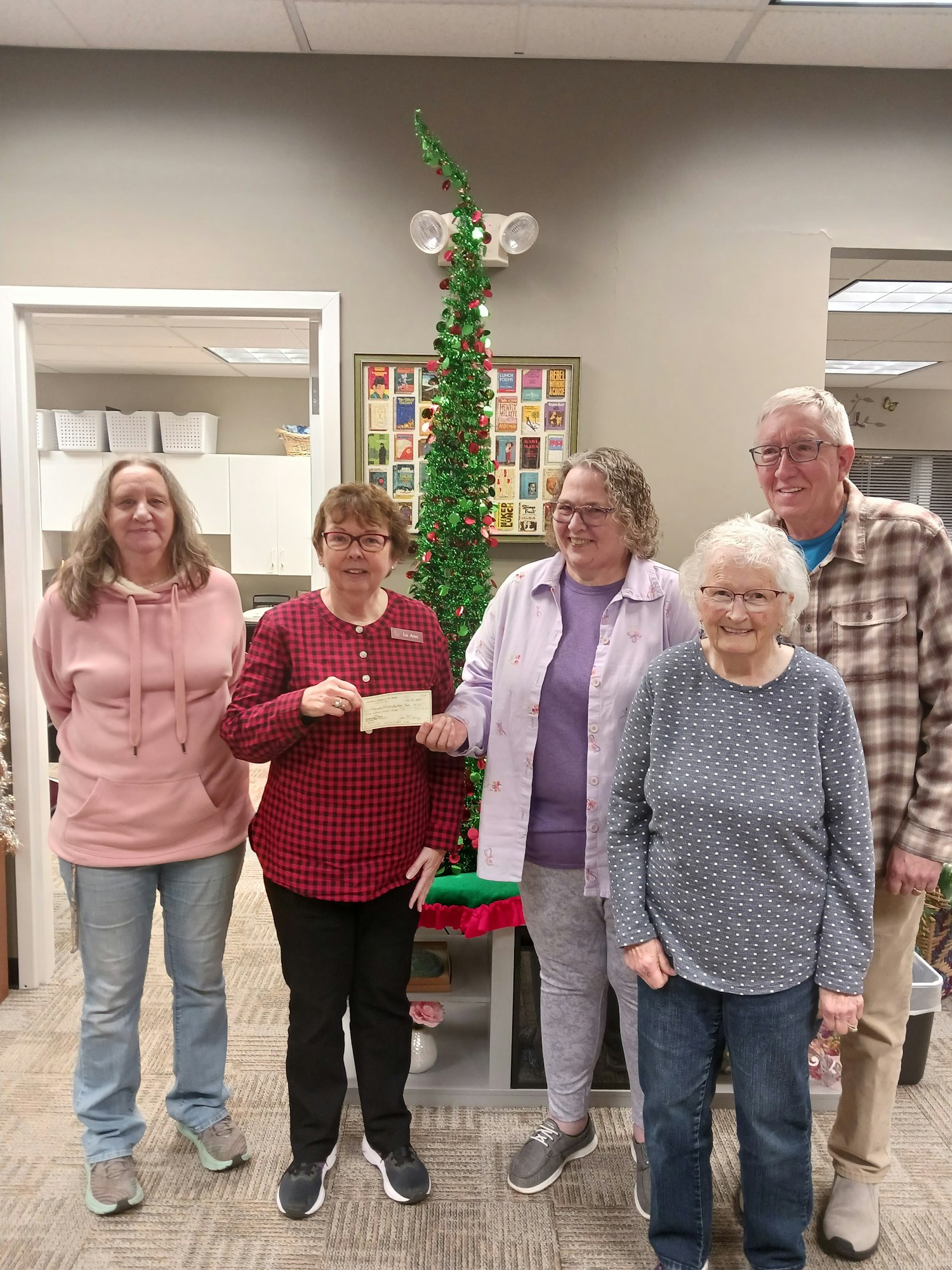 Five people posing in front of a Christmas tree, with one holding a check.