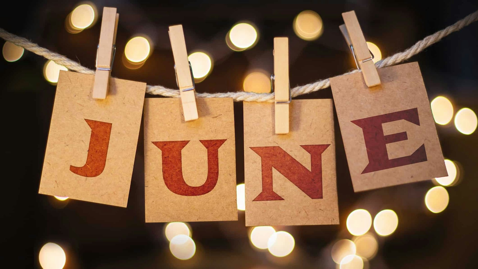 The word "JUNE" on cards clipped to a rope with bokeh lights in the background.