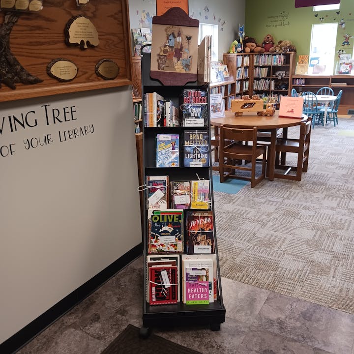 Library corner with bookshelves, tables, chairs, and a display rack with various books.