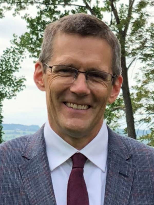 A smiling man with glasses wearing a suit and tie outdoors.