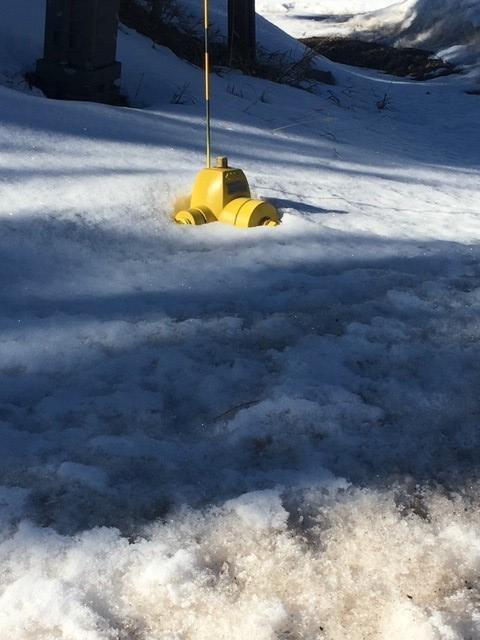 A yellow fire hydrant partly buried in snow, with a flagpole attached on top.