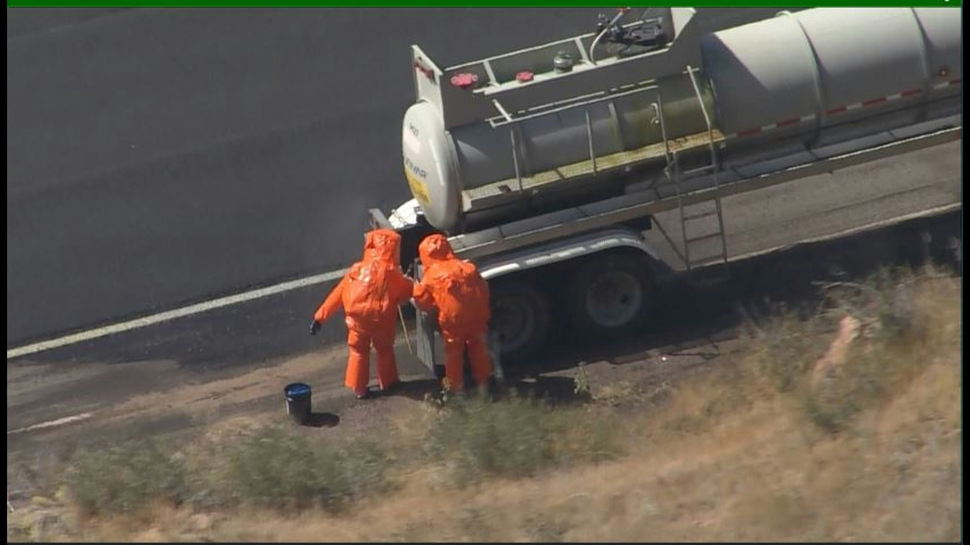 Two people in hazmat suits working near a tanker truck on the side of a road.