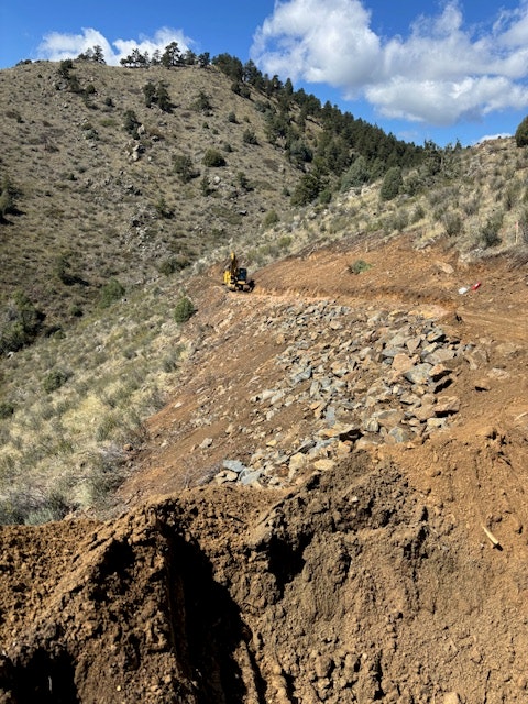 A construction site on a rocky hill with machinery, dirt, and a clear blue sky.