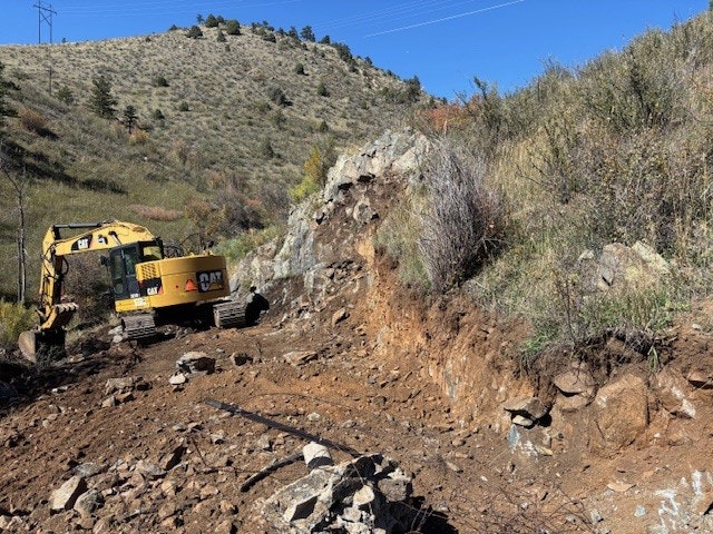 An excavator on a rocky hillside under a clear blue sky.