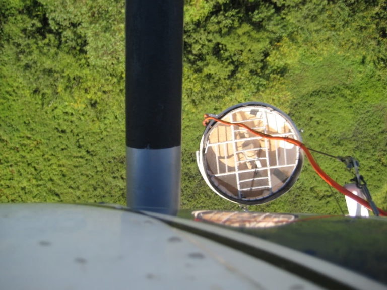 View from a height showing a round radar or satellite dish and cables, against a background of green foliage.