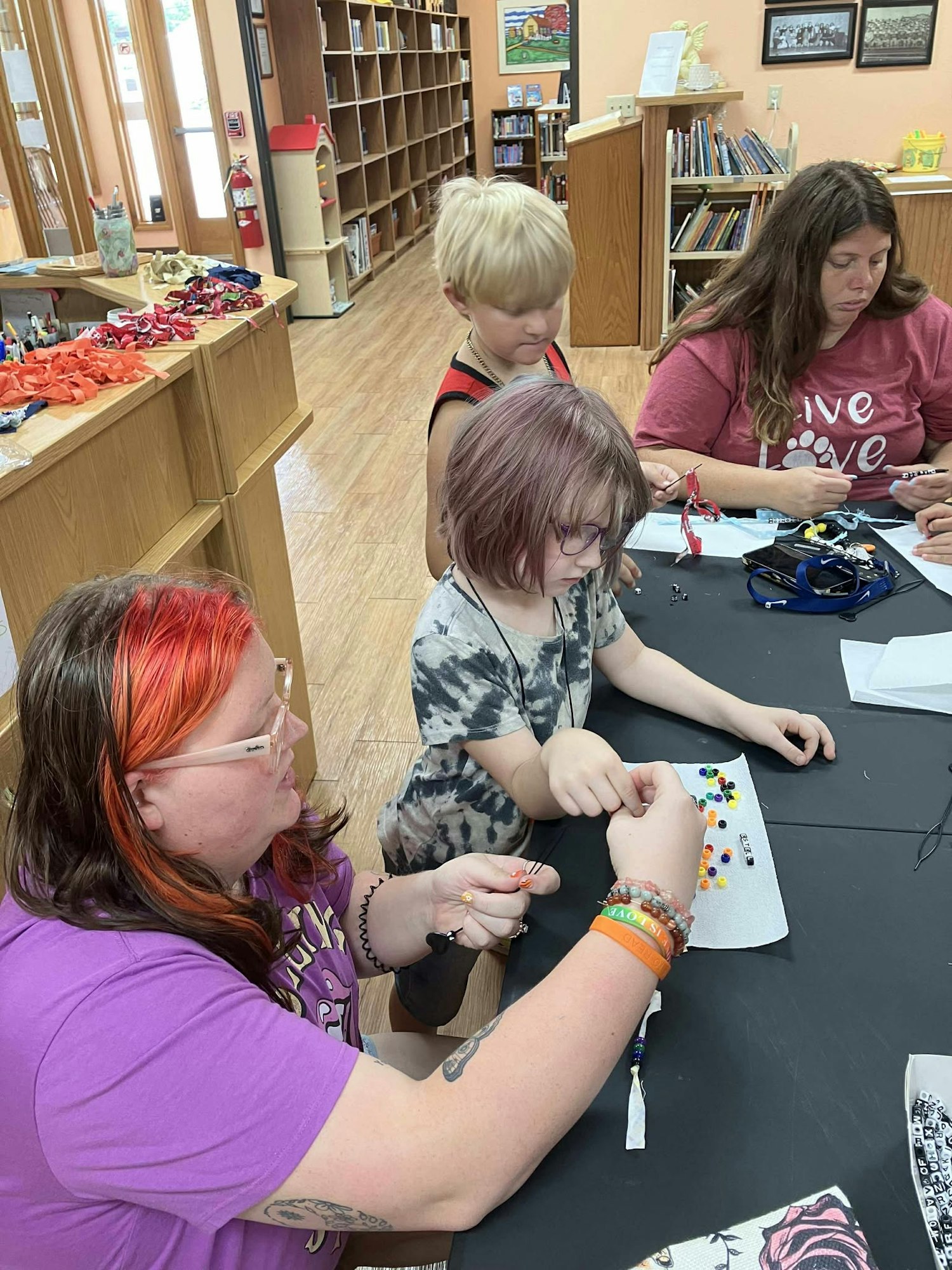 People making crafts with beads at a table in a library.
