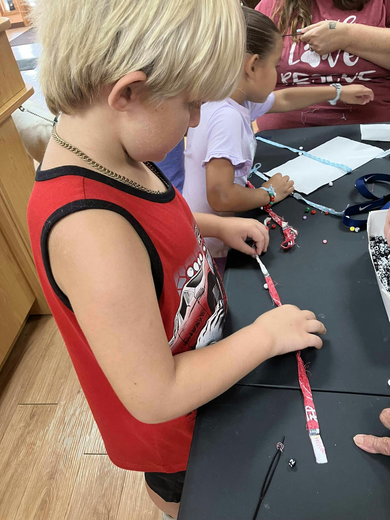 Two children making crafts at a table with beads and string.