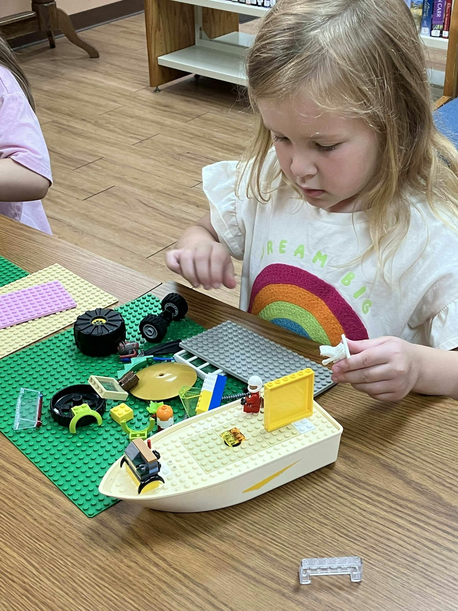 A child is playing with LEGO building blocks on a table, creating a boat and other structures.