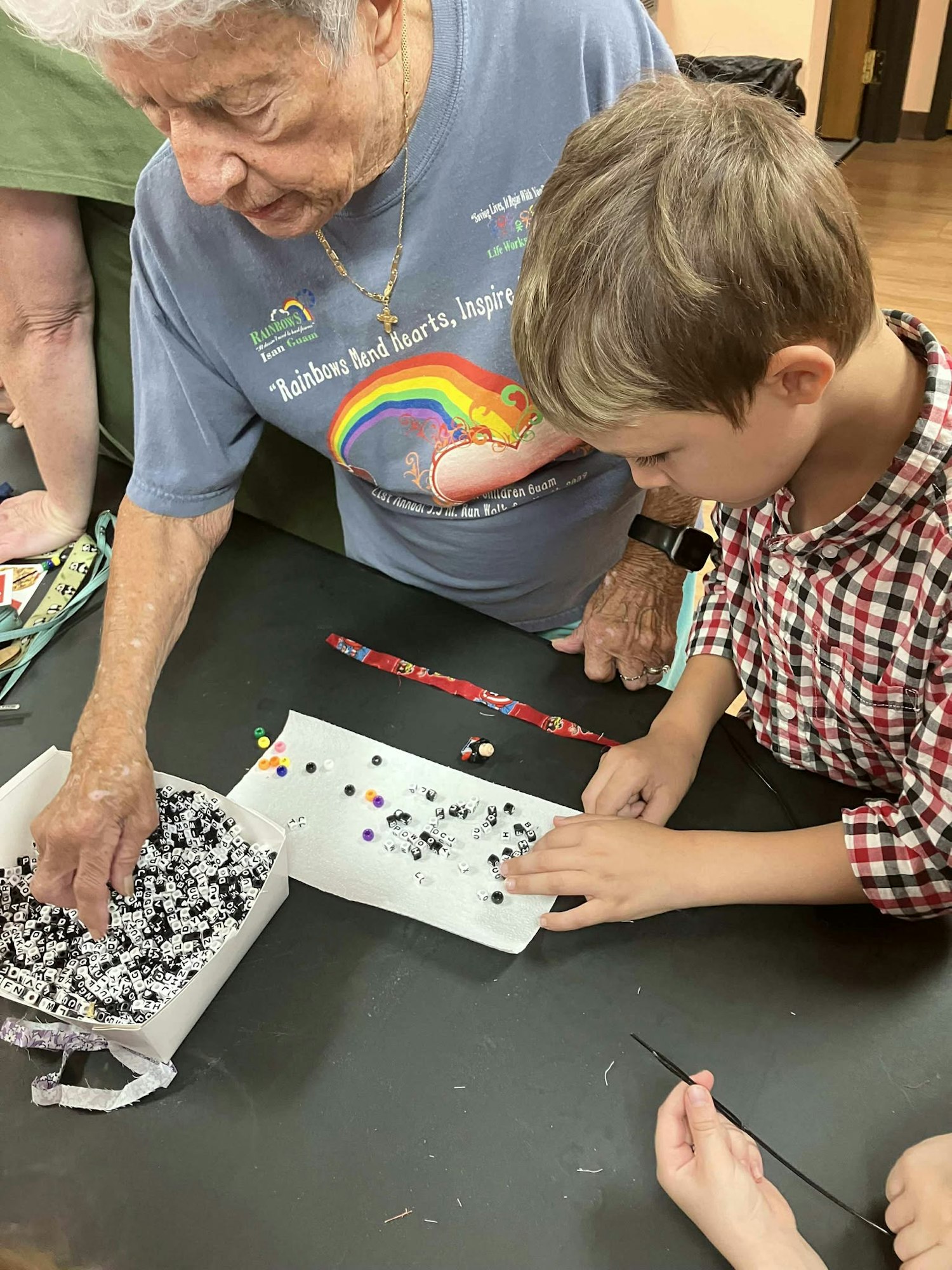 An elderly person and a child are sorting alphabet beads on a table.