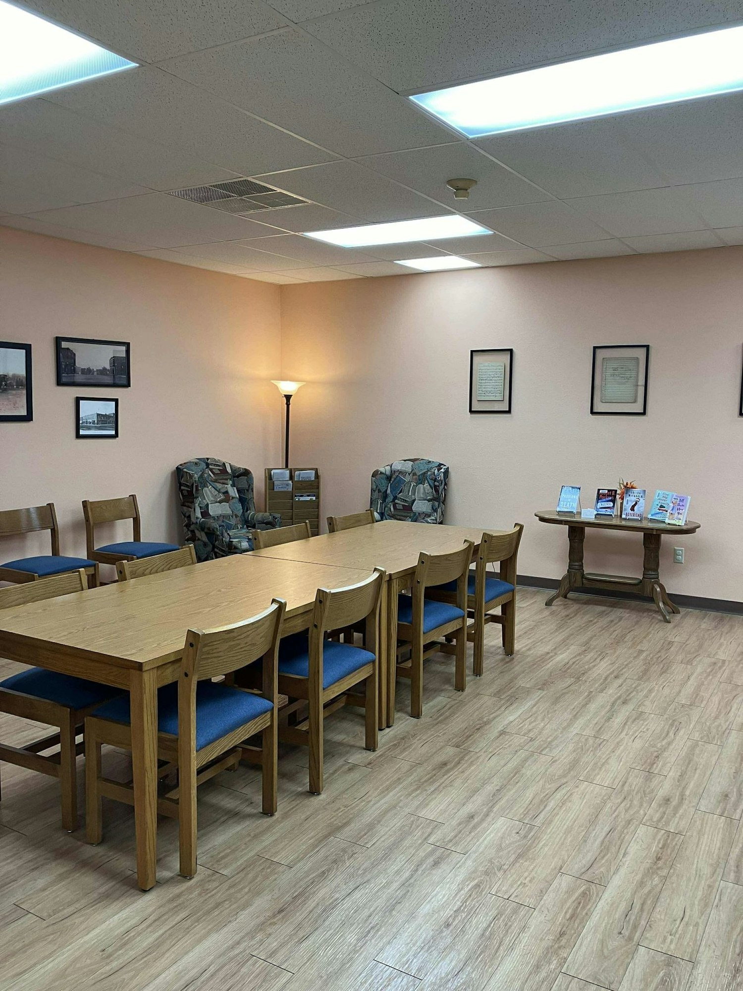 A well-lit room with tables, chairs, framed pictures on the wall, and a floor lamp.