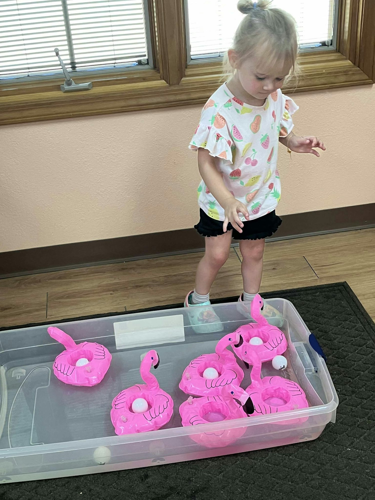 A child stands by a box with toy pink flamingos and white balls in water.