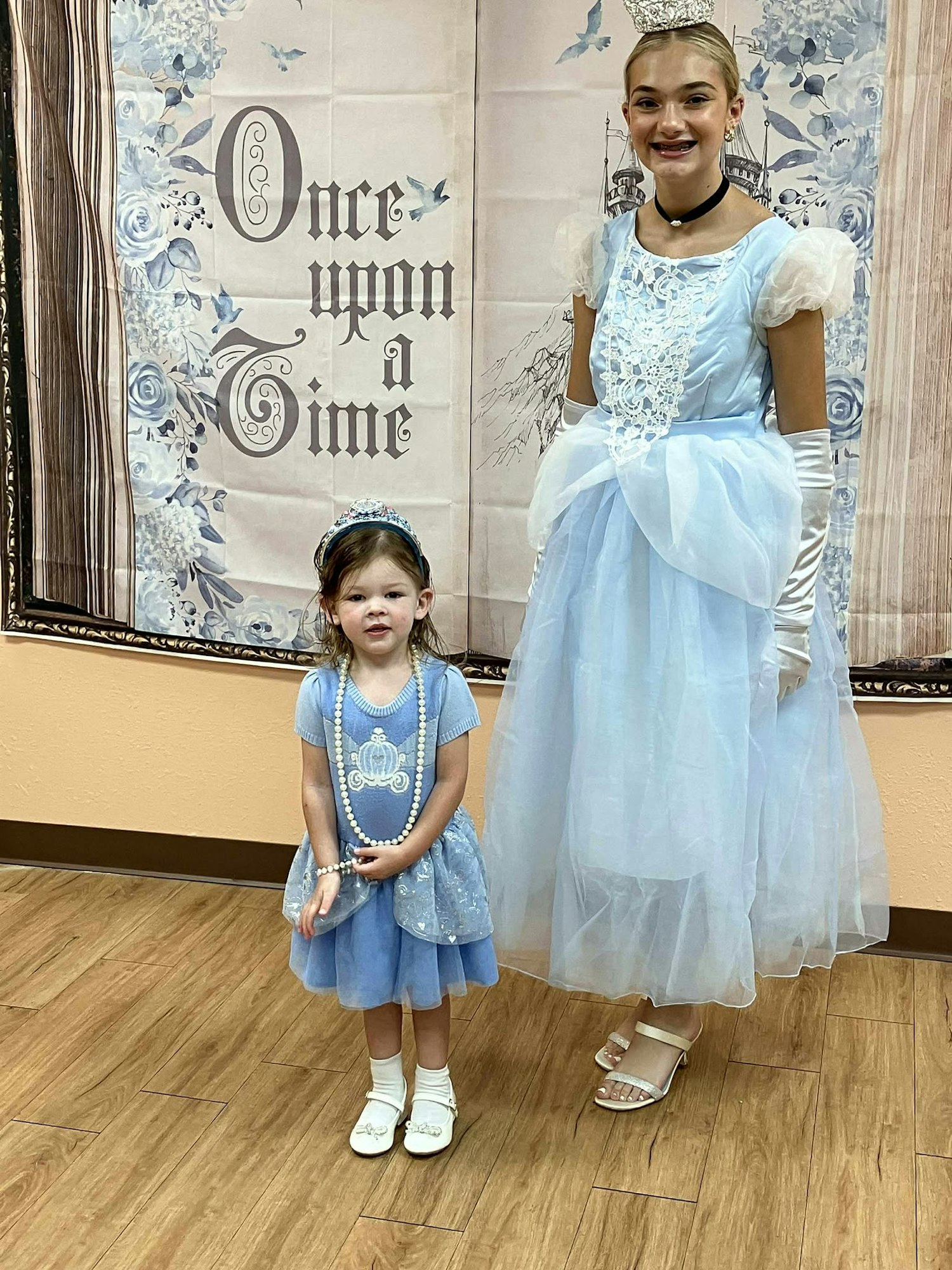 Two people in blue dresses, one child and one adult, pose in front of a "Once Upon a Time" backdrop.