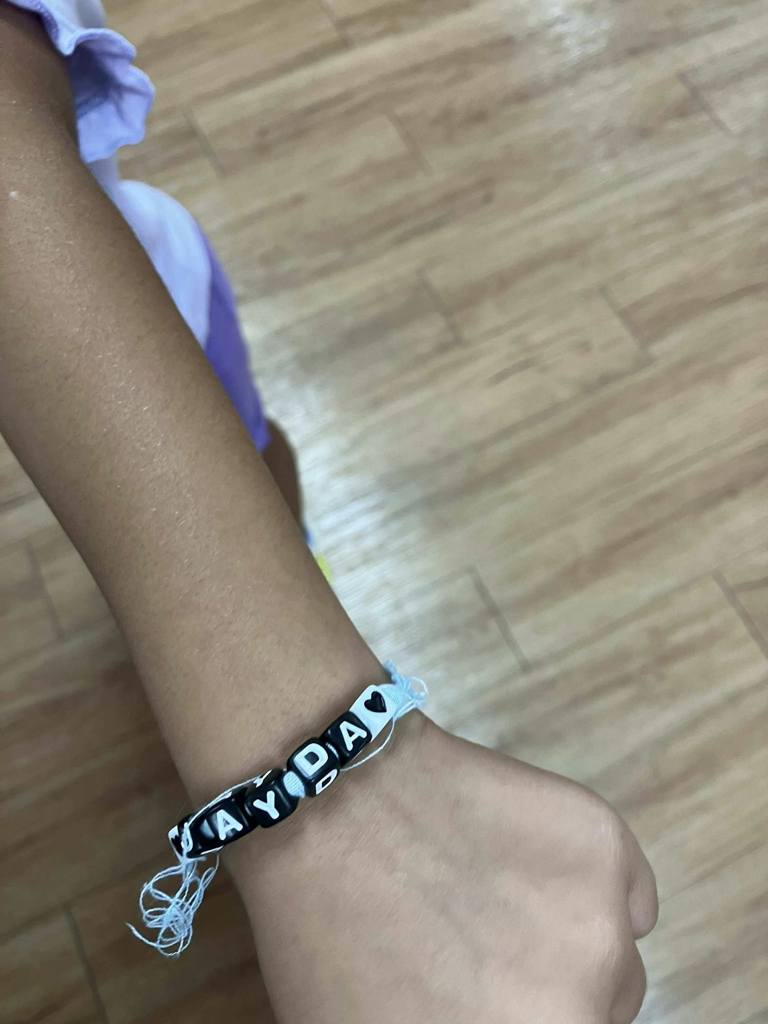 A handmade bracelet on a wrist with the name "JAYDA" and heart beads, on a wooden floor background.