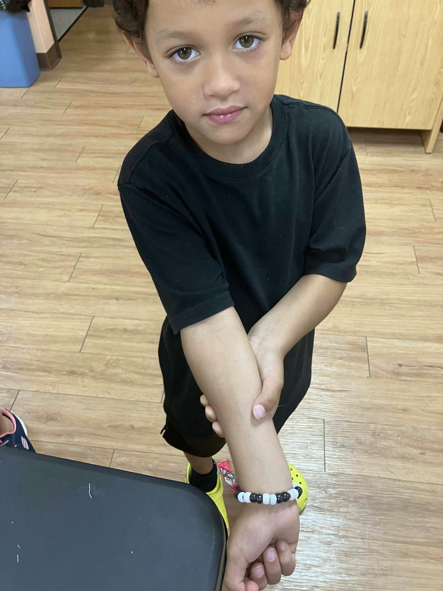 A child in a black shirt shows an arm with a beaded bracelet.