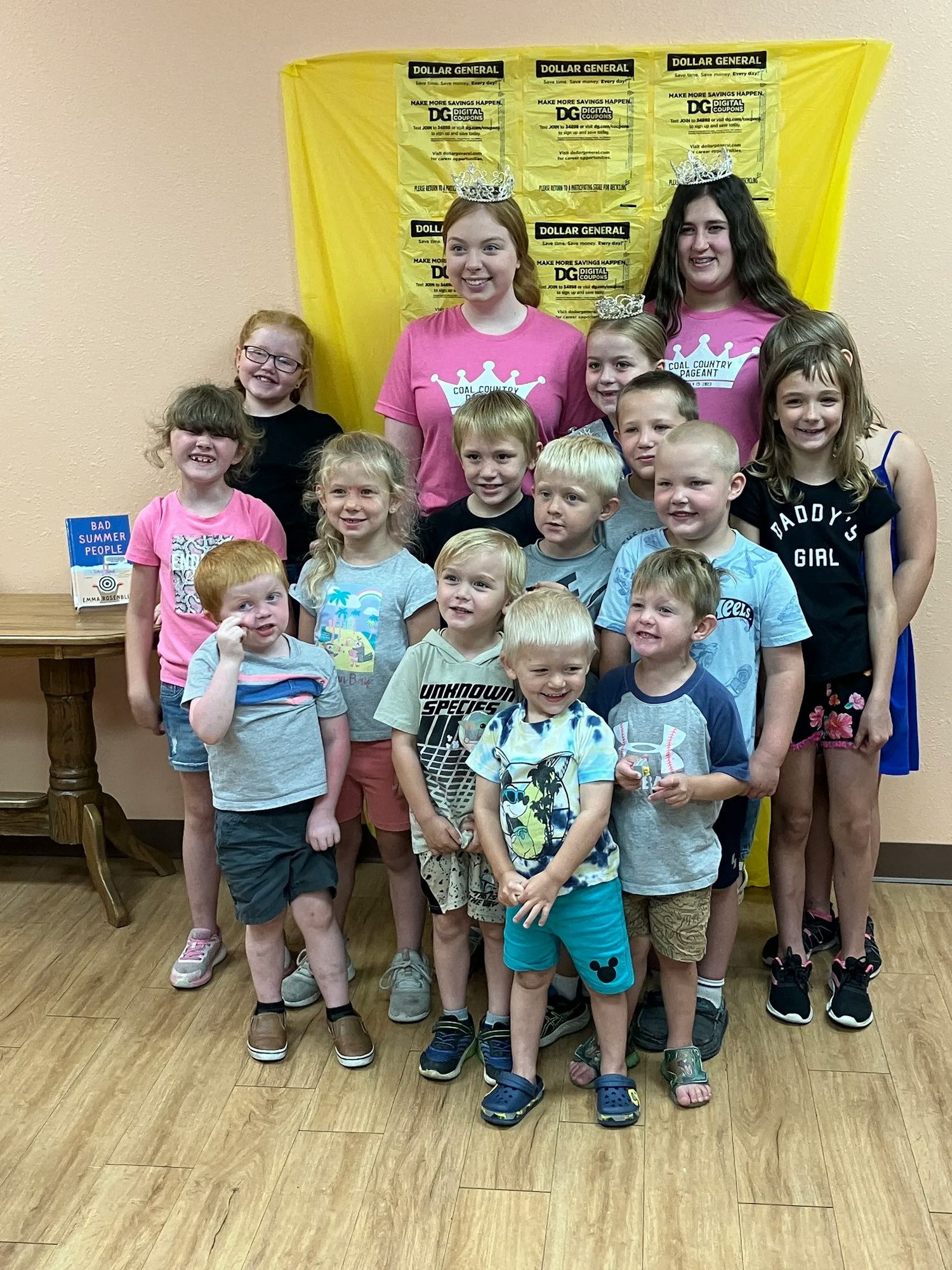 Group of kids with two adults at an event, posing for a photo, with a Dollar General backdrop behind.