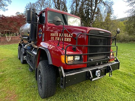 A red fire department water tanker truck on grass.