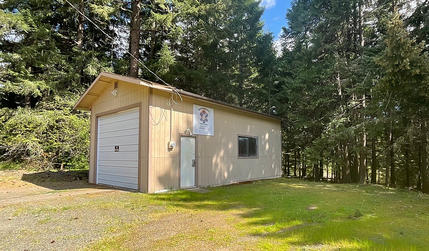 A small building with a garage door, surrounded by trees under a clear sky.
